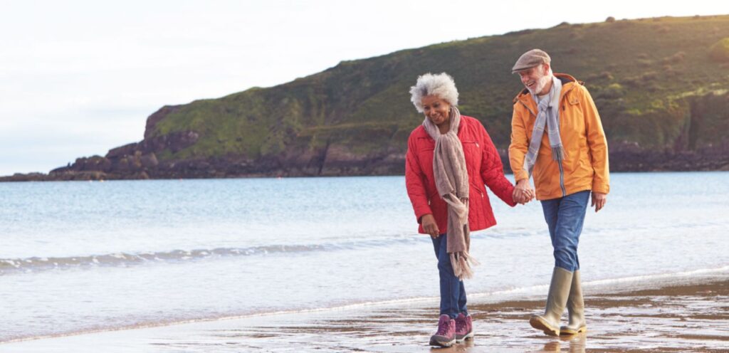 Senior couple holding hands and walking along shoreline.