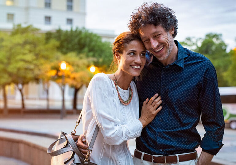 Happy married couple embracing and smiling while walking in a foreign city, representing U.S. expat married couples planning for the foreign earned income exclusion while living abroad