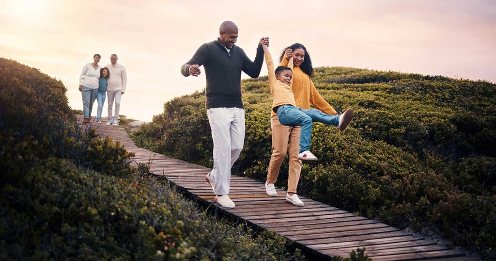 Multigenerational family walking and laughing along a wooden boardwalk in nature, representing legacy and estate tax planning