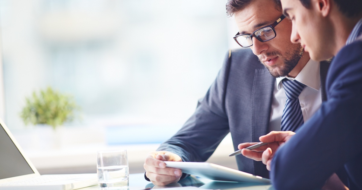 Wealth advisor meeting with a client in an office, reviewing a financial plan on a digital tablet.