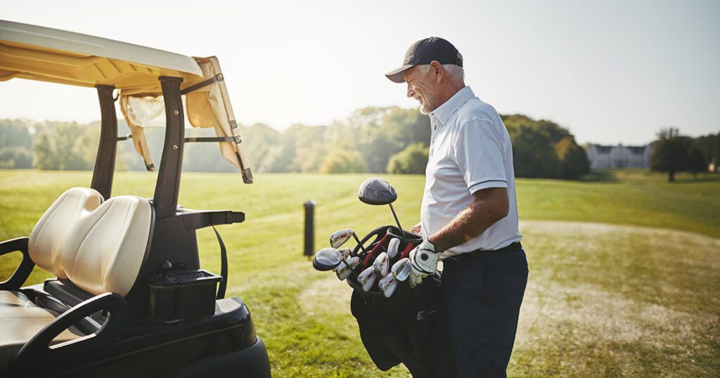 Retiree standing beside a golf cart and holding a bag of clubs on a sunny course, representing an active lifestyle and healthy habits that support a fulfilling retirement