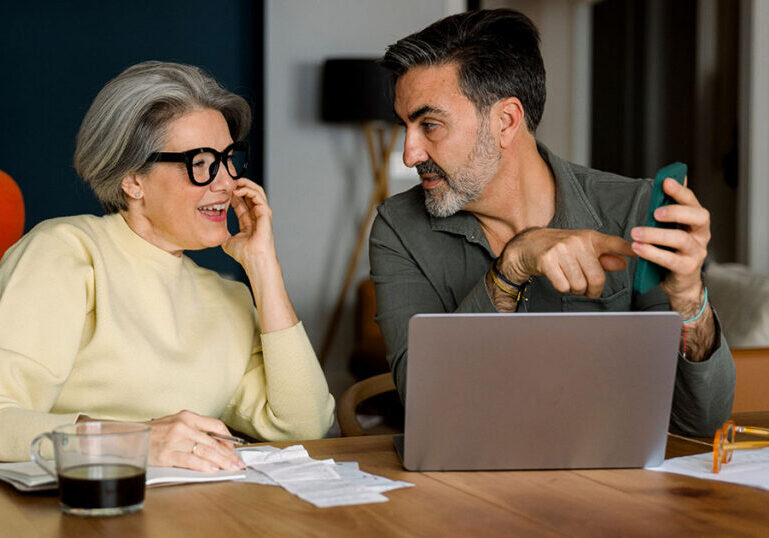 Couple reviewing bills and checking finances on a laptop at the kitchen table, illustrating how to organize your finances and get your financial house in order