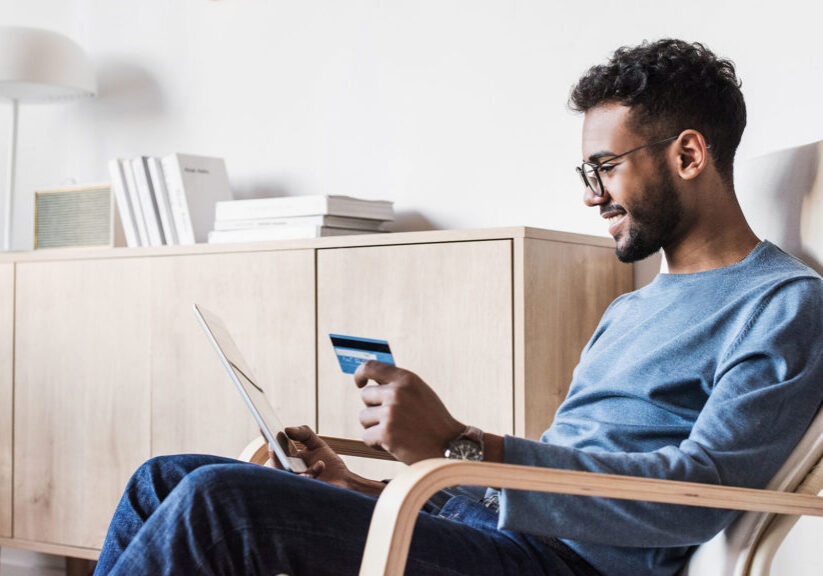 Young man holding credit card while reading on laptop