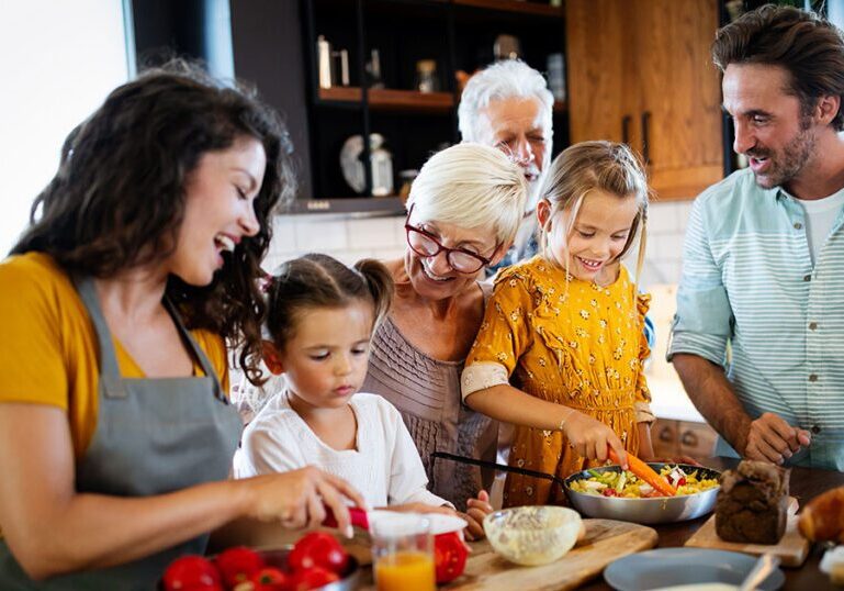 Multigenerational family preparing a meal together in the kitchen, representing coordinated family office risk management strategies to protect and preserve family wealth across generations