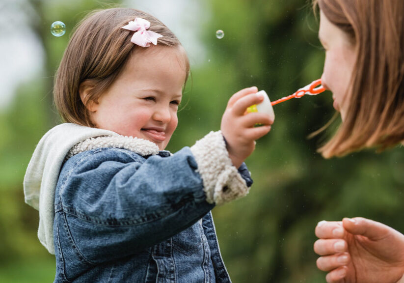 autistic child holding bubble wand near face of woman in park