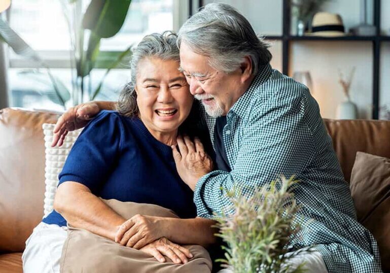 A happy retired couple laughing together on a couch in a comfortable, modern home.
