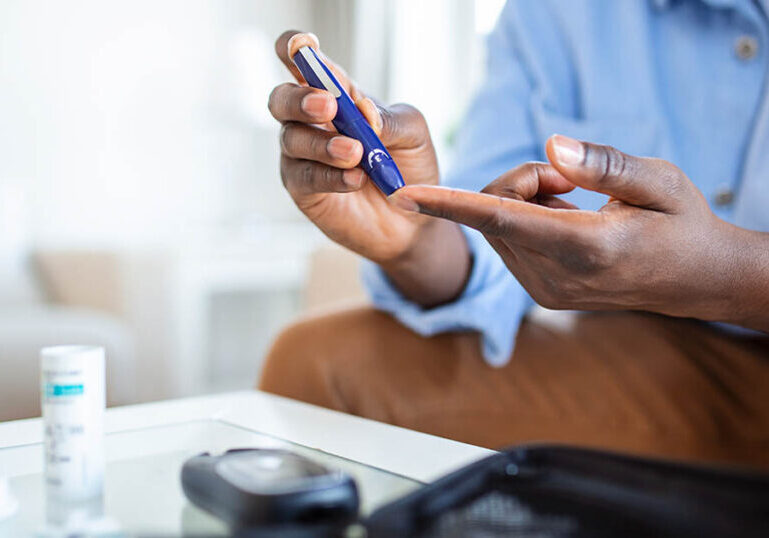 man sitting on sofa testing his glucose levels as he deals with chronic illness