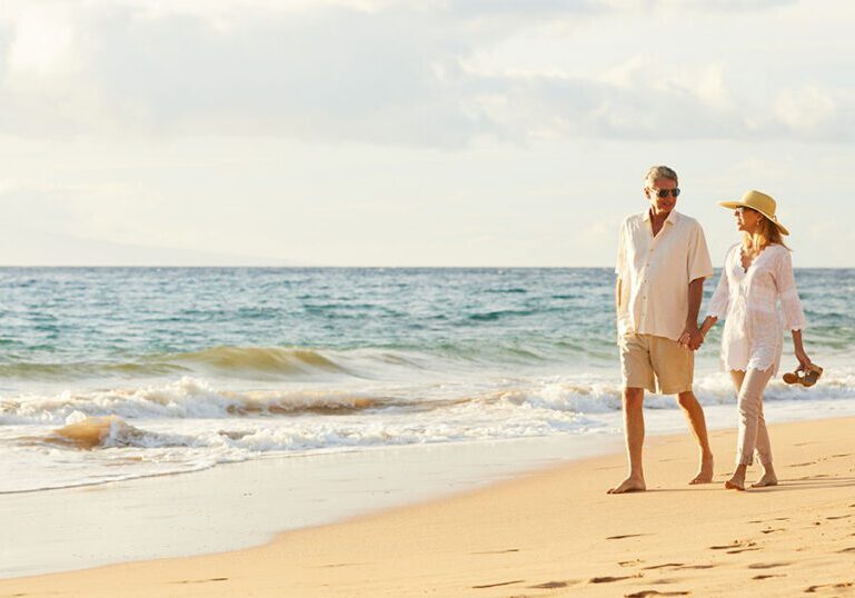 Married couple walking hand in hand along a sunny Florida beach, representing the estate planning and tax benefits a Florida Community Property Trust can offer married couples
